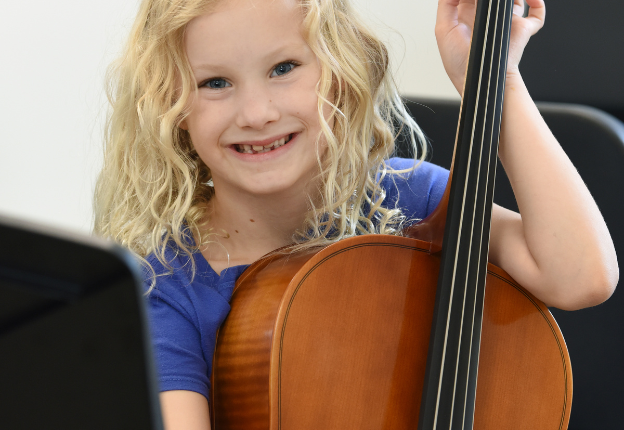 Young girl with a big smile posing for picture with cello